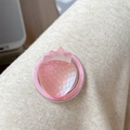 Close-up of a pink resin strawberry phone socket grip on beige knit fabric - Iridescent Strawberry-Red