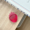 Detail of a bright red strawberry-shaped phone grip on a natural wood surface - Iridescent Rose Red