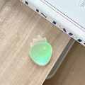 Detailed view of a semi-transparent green strawberry phone grip with scale texture on a table - Iridescent Light Green