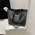 Gesteppte schwarze Denim-Tragetasche mit Logo auf einem weißen Koffer präsentiert - Schwarz