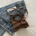 Brown leather handbag with large bow ornament and twisted handle on soft beige bedding - Brown