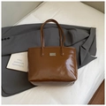 Detailed close-up of brown glossy leather tote bag with silver plate on a gray blazer - Brown No Pendant