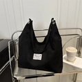 Minimalistische schwarze Canvas-Einkaufstasche mit Etikett auf modernem Metallregal - Schwarz