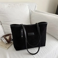Minimalist black corduroy tote bag with leather straps and logo label on a white sofa - Black