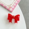 Detailed close-up of a red glossy bow phone grip with delicate gold emblem on white surface - Red