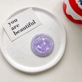 Close-up of a purple seashell textured MagSafe phone grip on a white ceramic plate - Magnetic Model / Purple