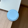 Close-up of a round light blue silicone phone socket grip on a wooden desk corner - Blue