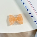 Close-up of peach glitter bow phone grip with MagSafe magnetic base on white surface - Pearl Adhesive Style / Orange