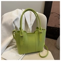 Détail du sac seau vert élégant avec boucles dorées posé sur une chaise crème - Vert