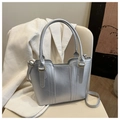 Détail du sac seau argenté métallisé avec coutures décoratives sur une chaise crème - Argent