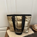 Bolso tote acolchado dorado metalizado con correas negras sobre un fondo de punto beige - Dorado