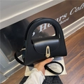 Minimalist black leather semicircular handbag with silver metal buckle in a casual cafe setting - Black