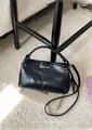 Detailansicht der schwarzen glänzenden Ledertasche mit Metall-Logo auf beigem Teppich - Schwarz