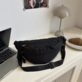 Minimalist black crescent crossbody bag with woven puller shown in a modern home office setting - Black
