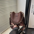 Dunkelbraune Leder-Eimertasche mit goldener Kette und gemustertem Gurt in der Hand - Braun