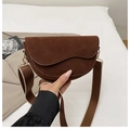 Close-up of a brown suede saddle bag with wave edge lid and a wide woven strap - Brown