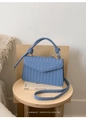 Detail of blue woven handbag with knotted handle on a wooden stool in a cozy setting - Blue