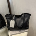 Bolso tote negro minimalista de cuero con adorno elegante sobre un podio blanco - Negro