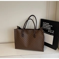 Dettaglio di una grande borsa tote marrone con motivo monogramma M su base di marmo - caffè