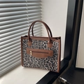 Leopard print tote bag with brown handles and front zipper on a sunlit windowsill - Gray