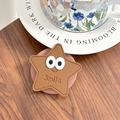 Détail du support téléphone étoile marron avec gaufrage Smile sur fond bois sombre - Marron