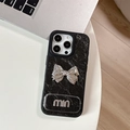 Detalle de funda de cuero negro con lazo de metal plateado y letras metálicas en 3D - Textura Nacarada De Agujeros Grandes - Soporte De Espejo A Juego - Mini Lazo - Negro / iPhone 17 Pro Max