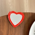 Macro detail of red glitter heart phone grip with mirror and 'mi ne.' logo on wood - Red