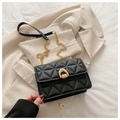 Detail of black quilted leather crossbody bag with golden horseshoe clasp on beige blazer - Black