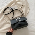 Minimalistische schwarze Leder-Umhängetasche mit großer Silberschnalle vor hellem Grund - Schwarz