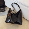 Glossy black crescent shoulder bag with metallic charms and fashion logo on sofa - With Charm / Black
