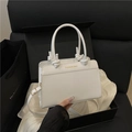 Minimalist white leather tote bag with gold logo and round handle being held by hand - White