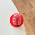Nahaufnahme einer rosa Bären-Handyhalterung aus Harz mit roter Basis auf weißem Tisch - Dunkelrot