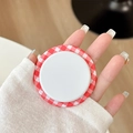 Close-up of red and white checkered magnetic pop-up phone grip held between fingers - Red