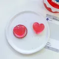 Detail showing two red heart-shaped resin phone grips on a decorative white plate - Transparent Stand / Matte Heart-Iridescent Ankara Red
