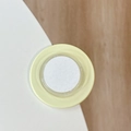 Close-up of a round yellow silicone corner protector with adhesive back on a white desk - Yellow