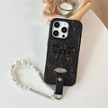 Detail of black faux leather phone case with polka dot bow and pearl lanyard strap - Black / iPhone 16e