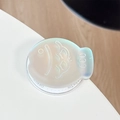 Detailed macro view of an iridescent fish-shaped phone air cushion stand on white desk - Magnetic Laser Taiyaki