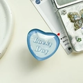 Detailansicht des hellblauen herzförmigen Griptok mit Lucky Day Text auf dem Tisch - Transparenter Ständer-Kristallglas Herz-Lucky Blau