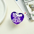 Detailaufnahme der herzförmigen Handyhalterung mit Love is in the air Aufdruck - Transparenter Ständer-Kristallglas Herz-Dunkellila Beschriftung