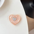 Dettaglio macro del supporto per telefono a cuore glitter pesca con emblema argento - Arancione Luccicante