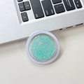 Macro shot of circular phone grip filled with light blue sequins on a desk surface - Green