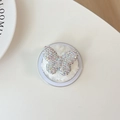 Macro shot of luxury butterfly phone grip with sparkling crystals on plush white padding - Plush Rhinestone Butterfly / Iridescent