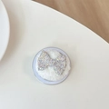 Close-up of sparkling AB rhinestone bow cell phone stand on a white plush base - Plush Rhinestone Flat Bowknot / Iridescent