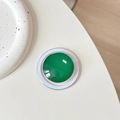 Close-up of a green crystal glass MagSafe phone grip on a white minimalist desk - Cyan Green