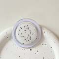 Detailed macro view of skincare cream with exfoliating particles in a purple rimmed jar - Magnetic Morandi Ink Splash White