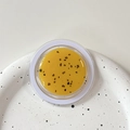 Overhead view of yellow glitter phone grip with black spots on a white speckled plate - Magnetic Morandi Ink Splash Ginger Yellow