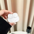 Close-up of a cute white acrylic frog phone grip accessory held in hand against curtains - White