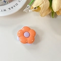 Close-up of a floral phone grip with orange petals and a purple center on a desk - Orange