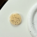Close-up of minimalist beige resin phone grip with black flecks on a white ceramic plate - Autumn Orange