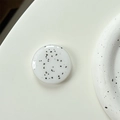 Detail der runden Handy-Halterung mit schwarzem Farbspritzmuster und glänzendem Finish - Weiß